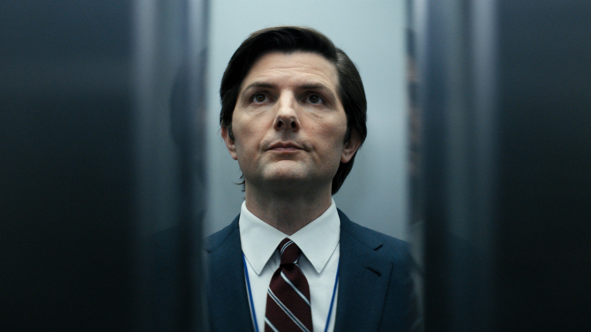 Severance: a man in a suit looks up in a dim elevator